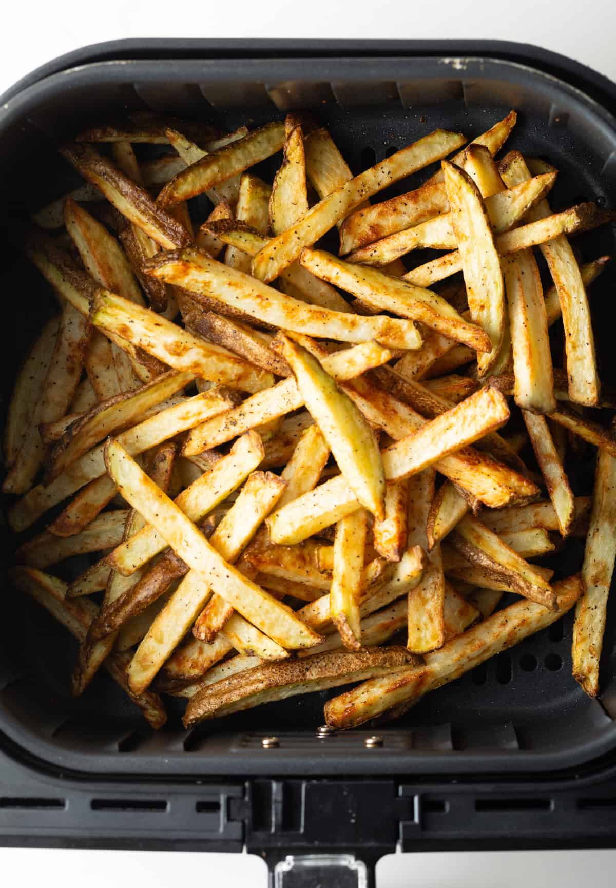 A batch of crispy air fryer fries sitting in an air fryer basket.