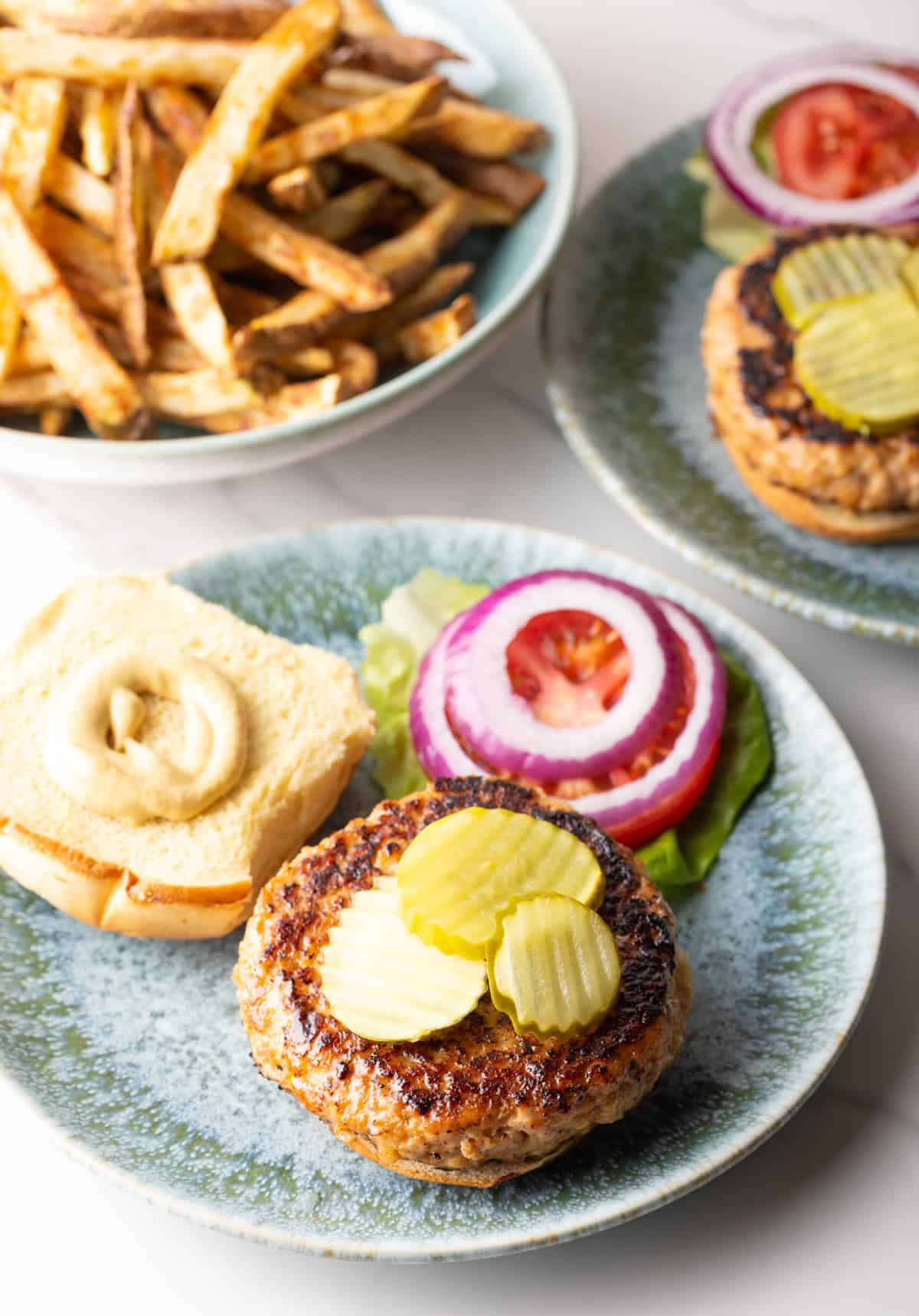 An open chicken patty sandwich topped with pickles, sitting on a plate with vegetable toppings.