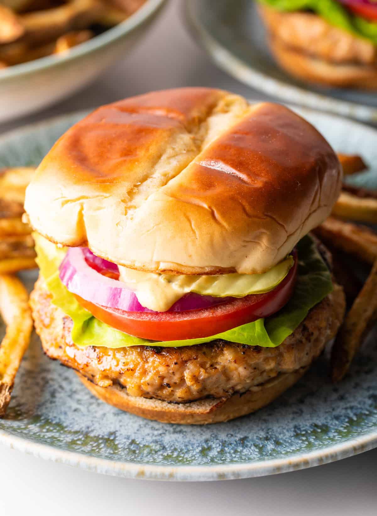 A chicken burger with ground chicken topped with condiments and vegetables between two hamburger buns.