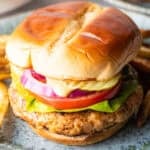A ground chicken burger topped with condiments and vegetables between two hamburger buns.
