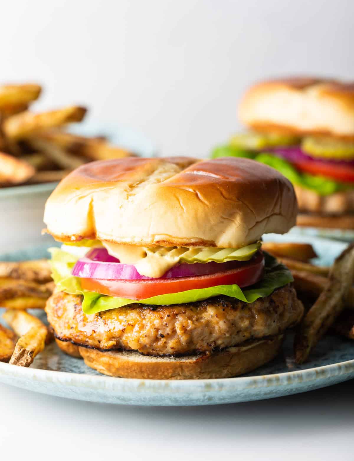 A bbq chicken burger sitting on a blue plate surrounded by fries.