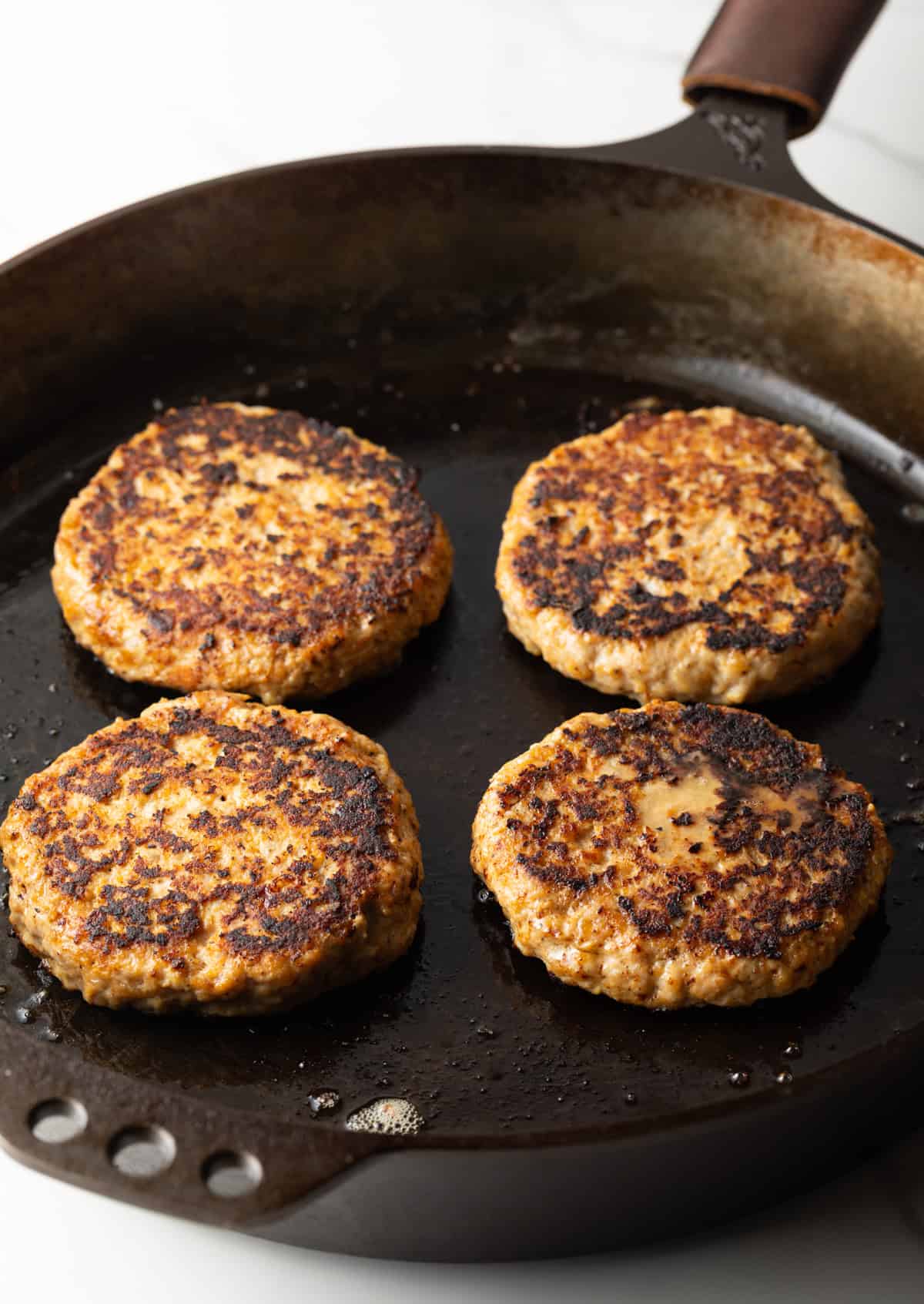 Four ground chicken burgers are being cooked in a black skillet.