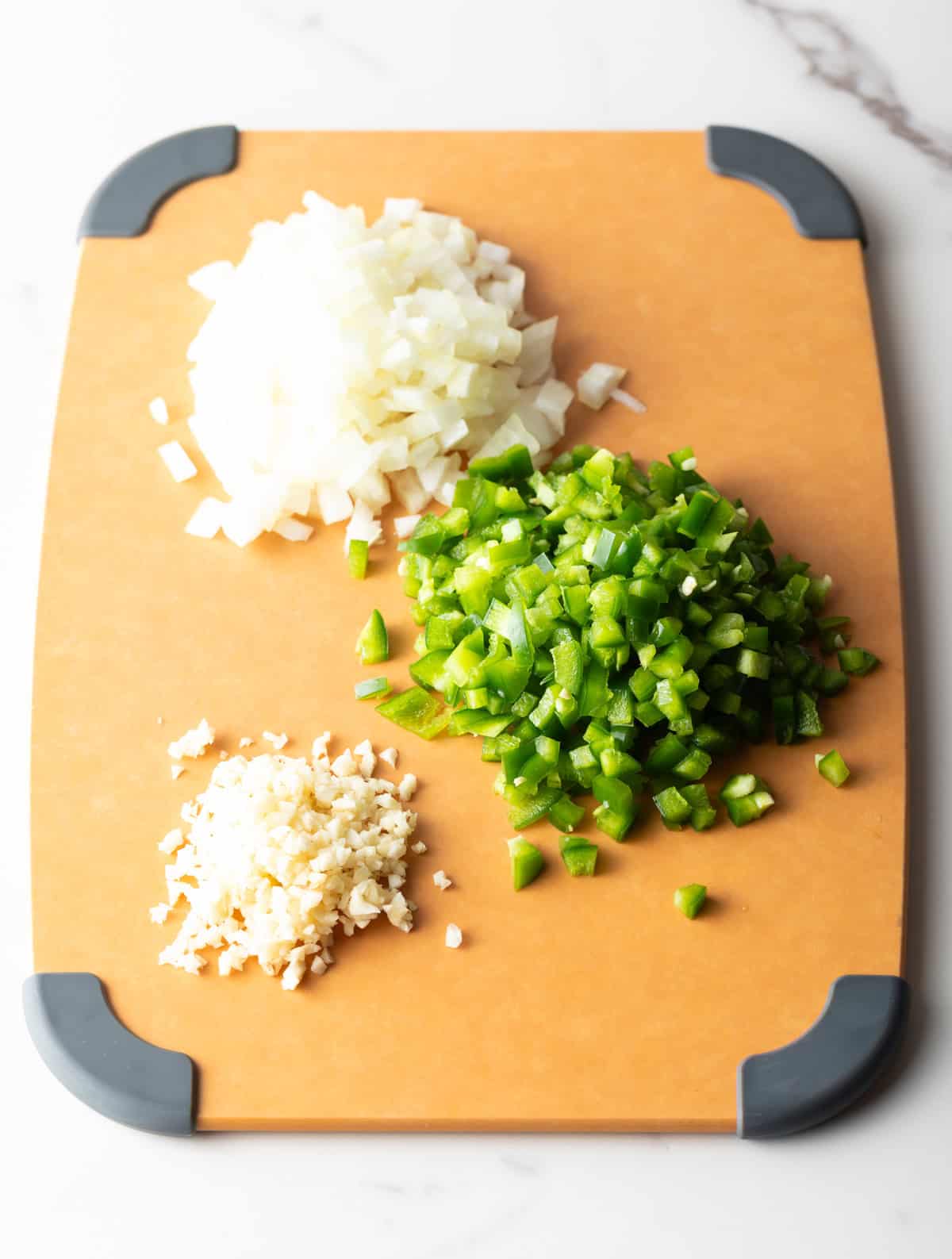 A cutting board topped with three piles of diced onions, jalapeños, and garlic.