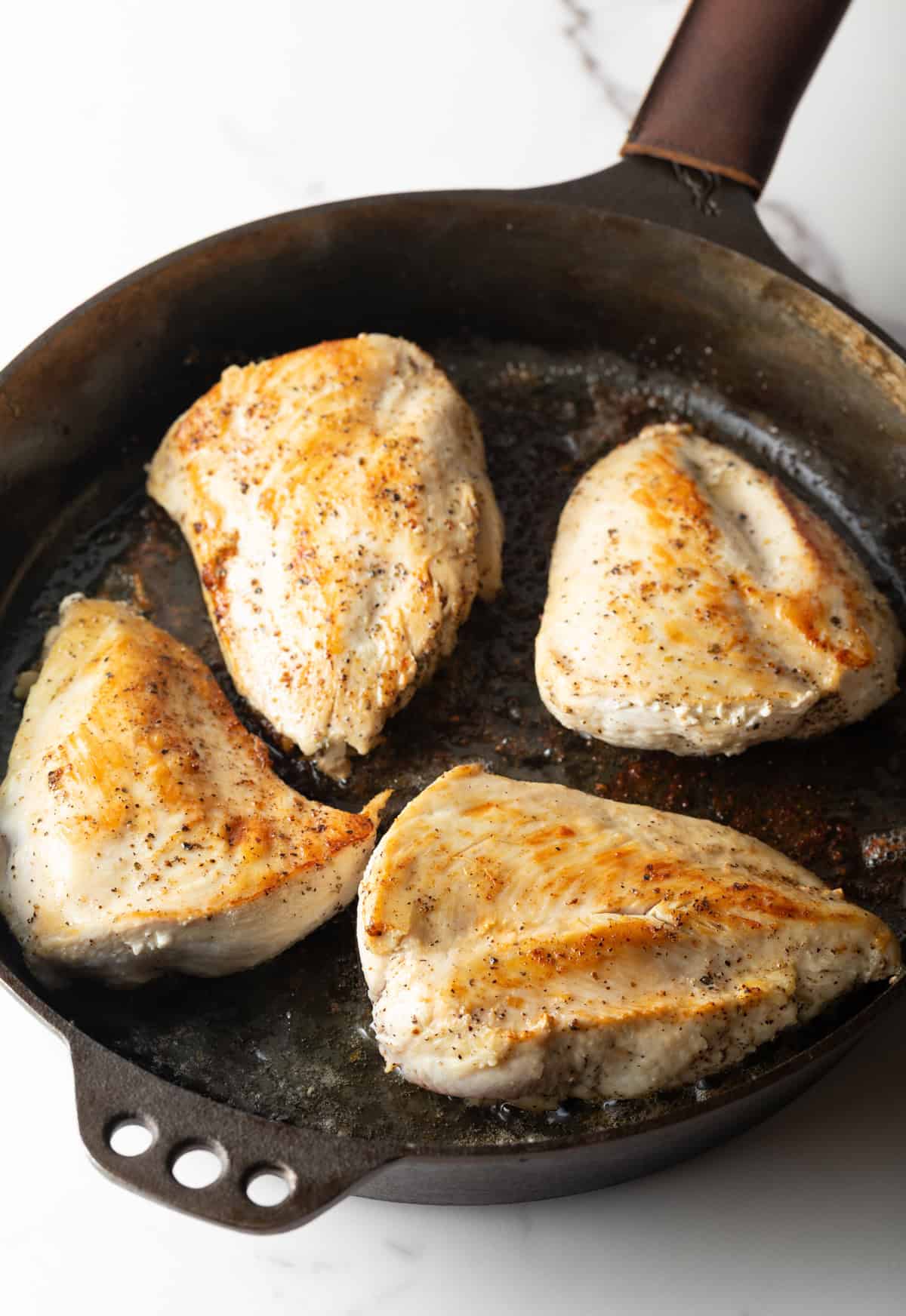 Four chicken breasts are being browned in a black skillet.