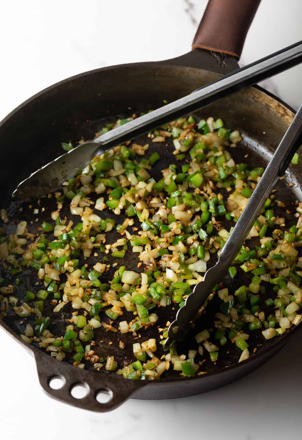 Diced jalapeño and onions are being sautéed in a black skillet.