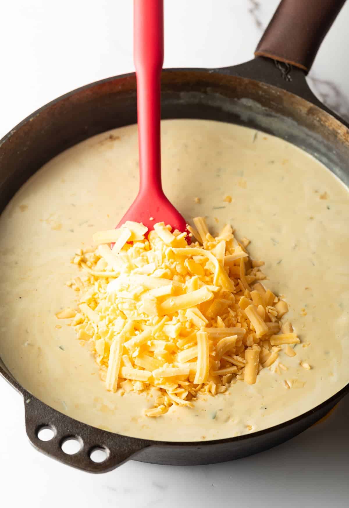 Shredded cheddar is being stirred into a cream mixture for jalapeno chicken.