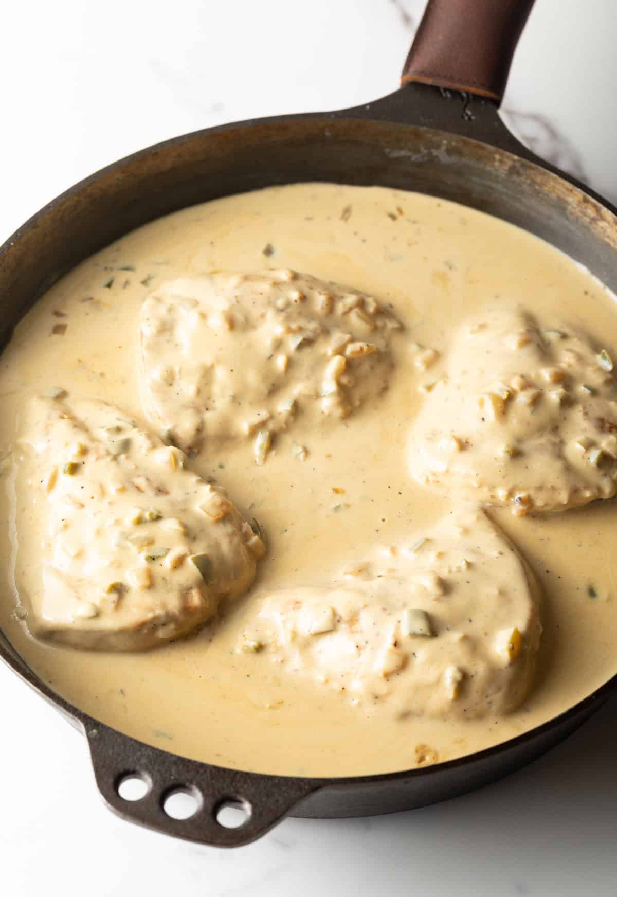 Chicken breasts are being coated with a creamy jalapeño mixture in a black skillet.