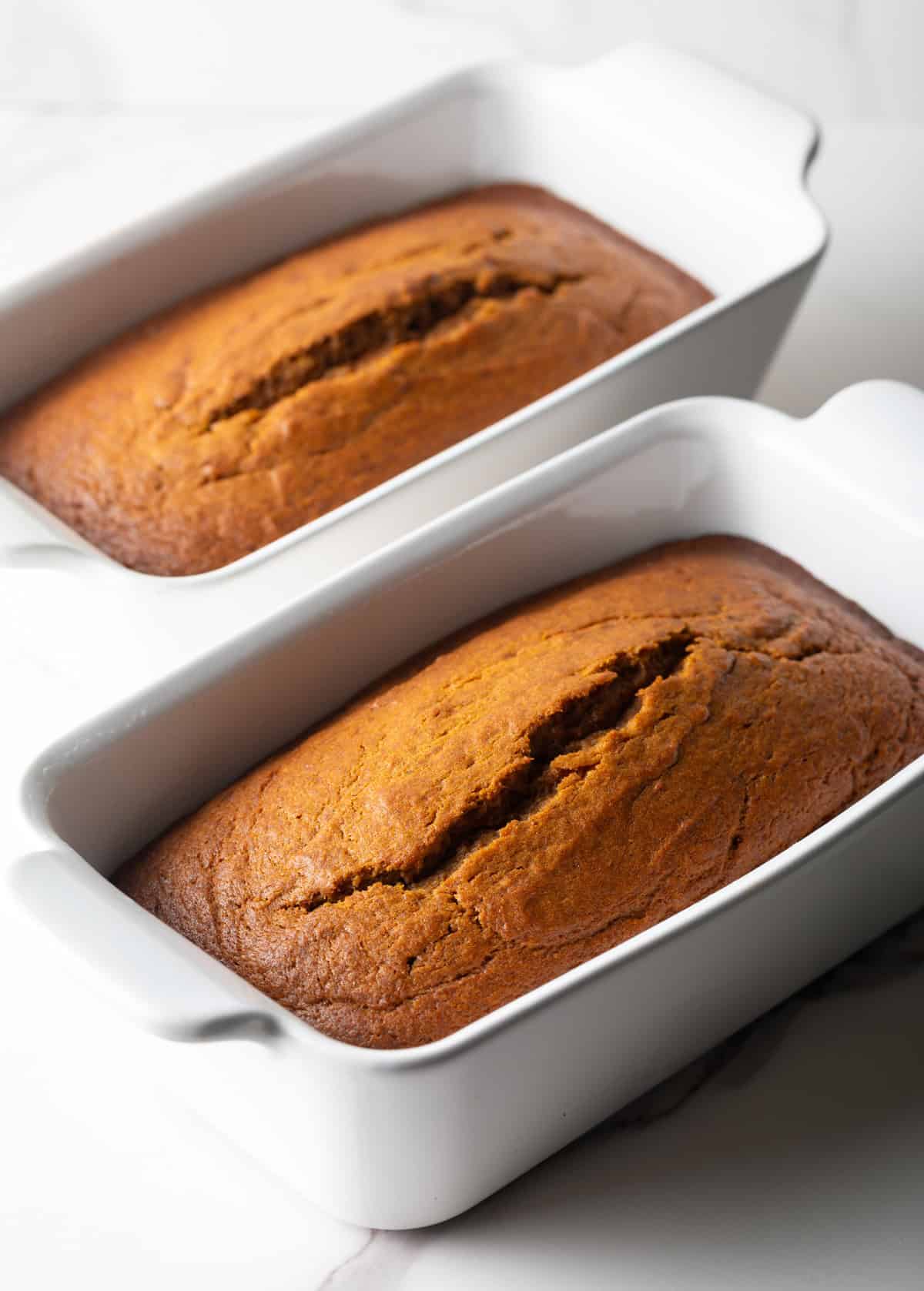An overhead shot of two loaves of easy pumpkin bread with canned pumpkin in white baking dishes.