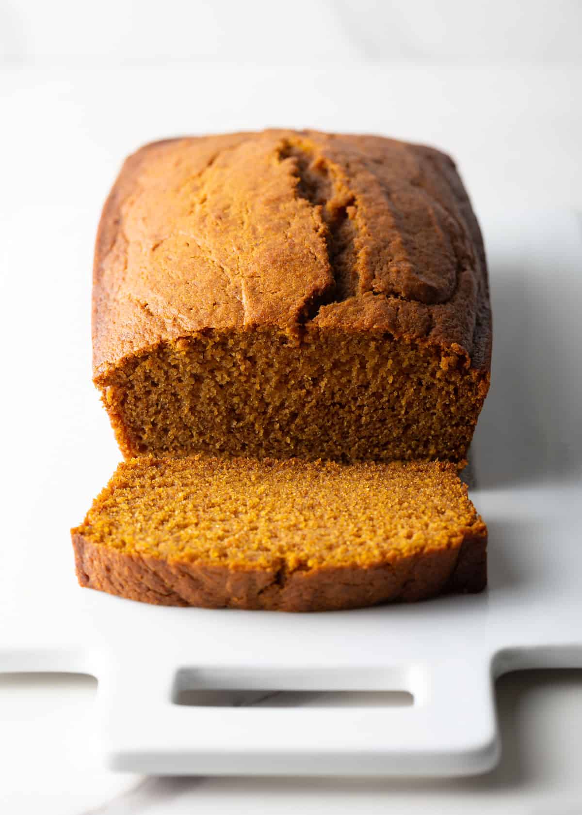 A moist pumpkin bread loaf with a single slice lying in front of the loaf.