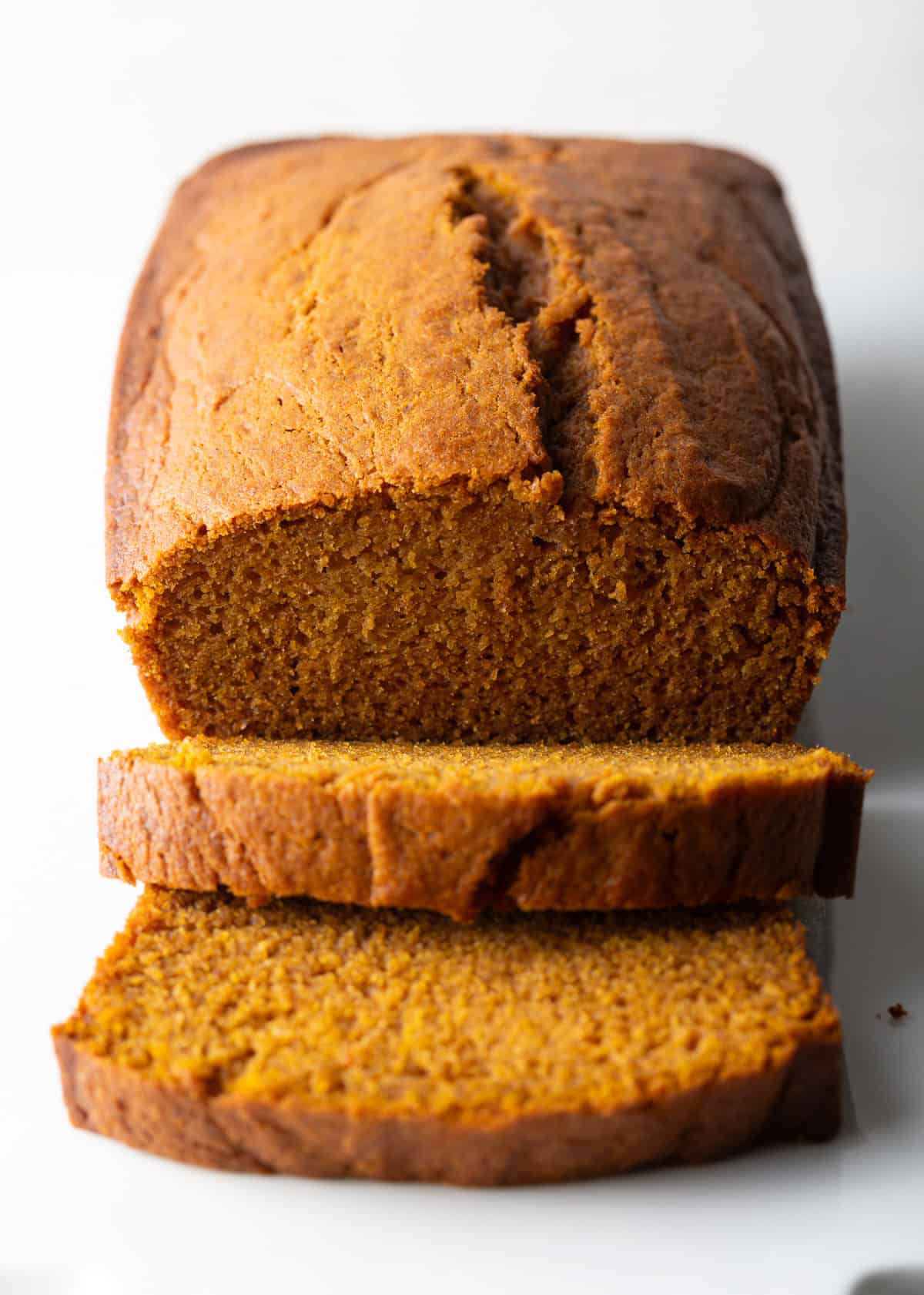 A loaf of an easy pumpkin bread recipe with two slices lying in front of the loaf.
