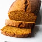 A moist pumpkin bread recipe with two slices stacked and laying down in front of the loaf.