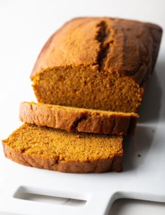 A moist pumpkin bread recipe with two slices stacked and laying down in front of the loaf.