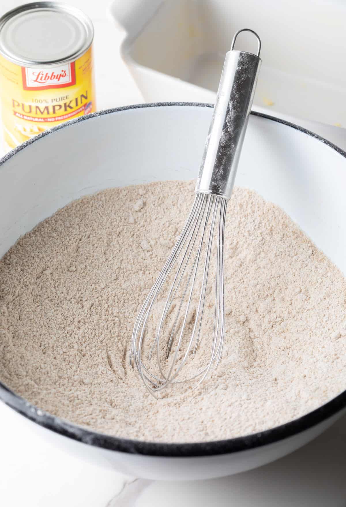 A flour and spice mixture for a moist pumpkin bread recipe is being whisked in a white bowl.