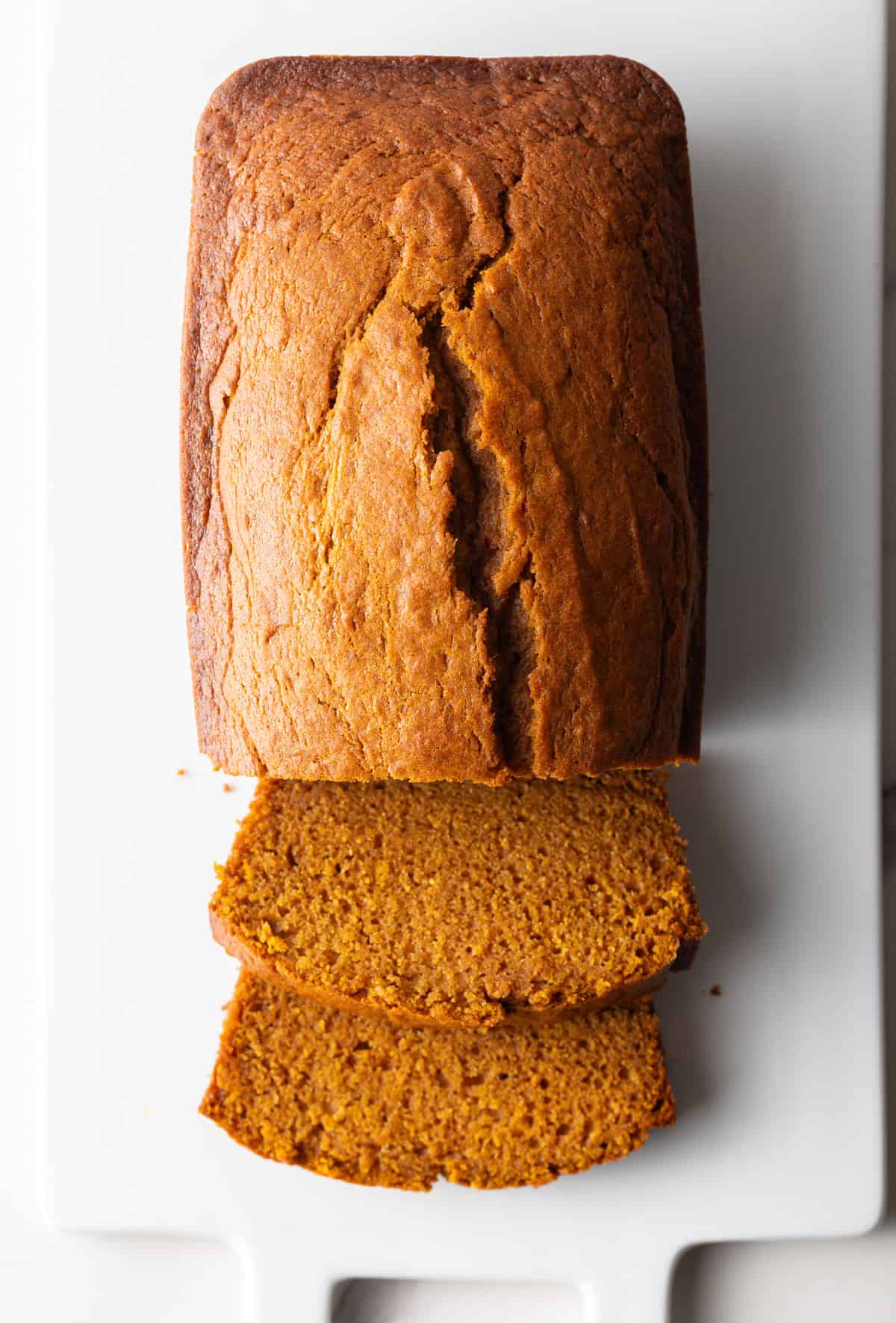 A top-down shot of a moist pumpkin loaf with two slices lying in front of the loaf.