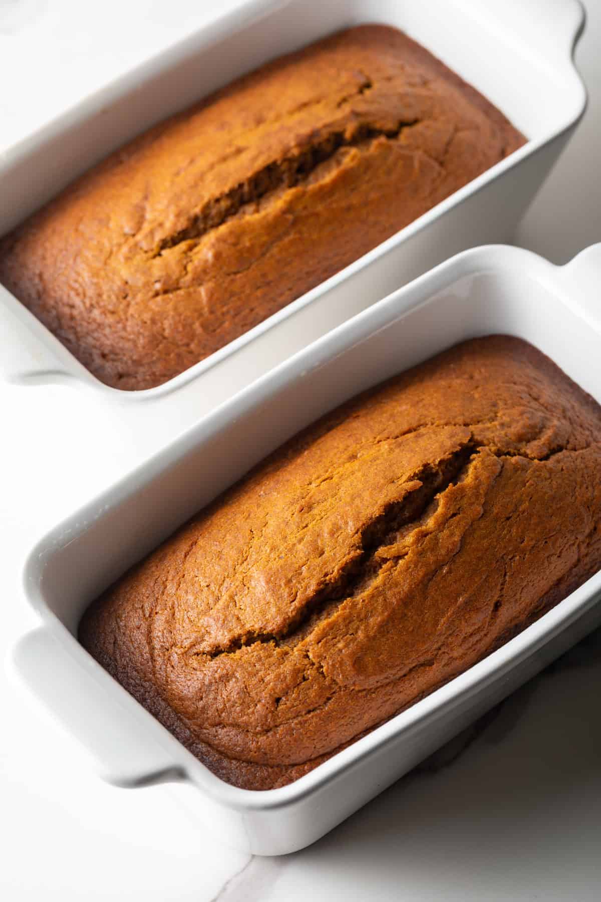 An overhead shot of two loaves of pumpkin spice bread in white baking dishes.