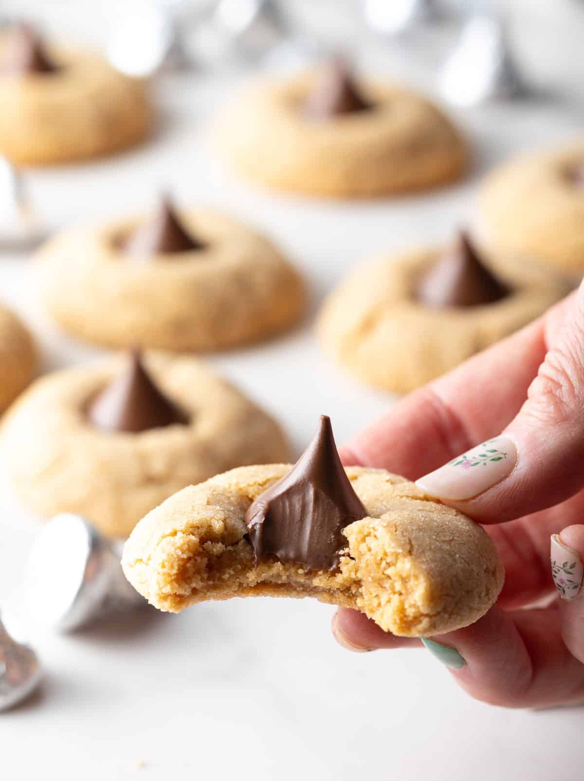 A hand is holding a peanut butter blossom cookie to the camera with a bite taken out.