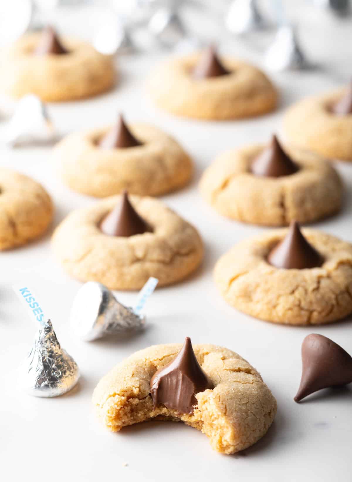 Peanut butter blossom cookies arranged on white parchment paper, and the cookie closest to the camera has a bite taken out of it.