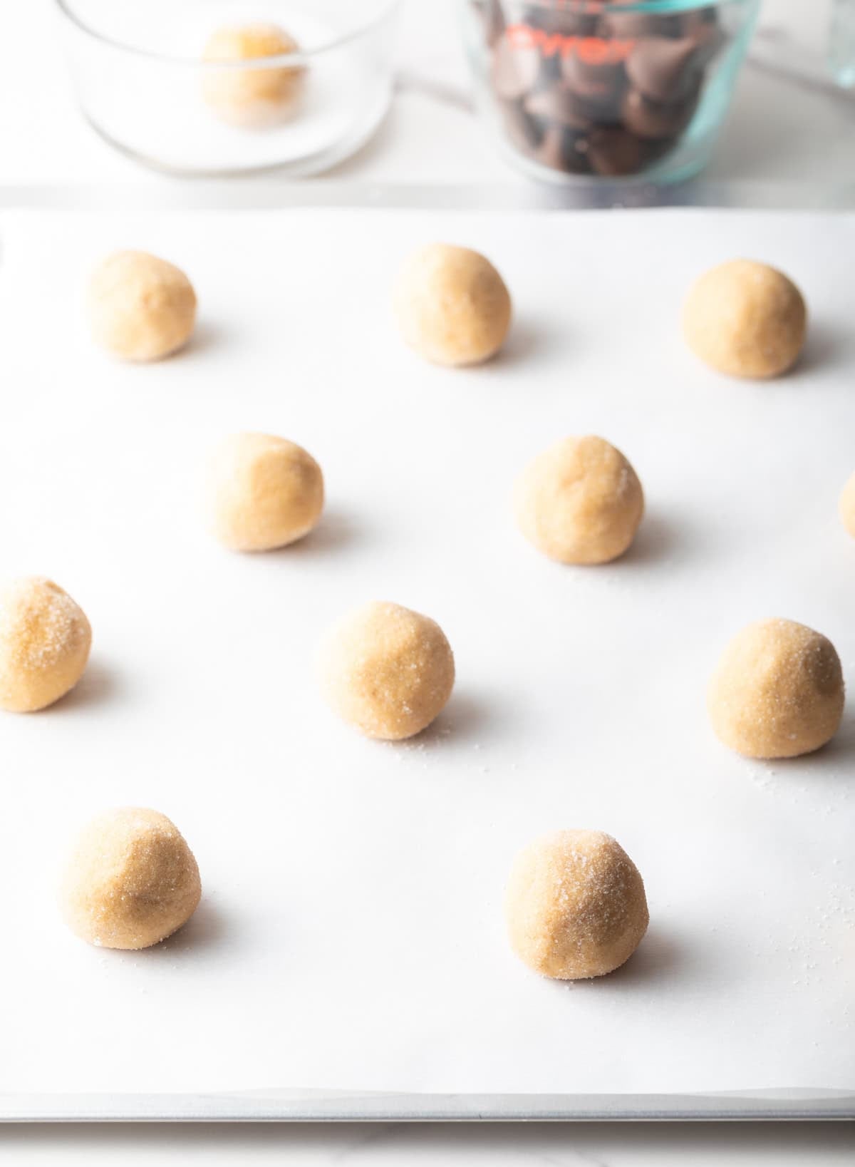 Raw peanut butter kiss cookie dough rolled into balls, sitting on white parchment paper.