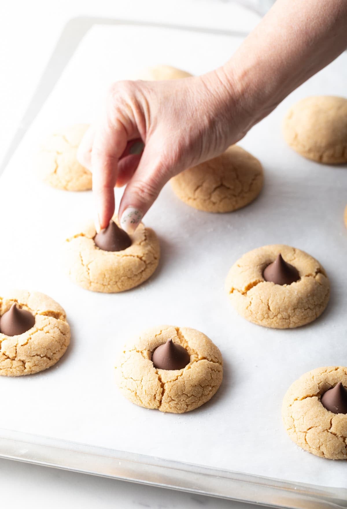 A hand is pressing a Hershey's Kiss into a peanut butter blossom cookie.