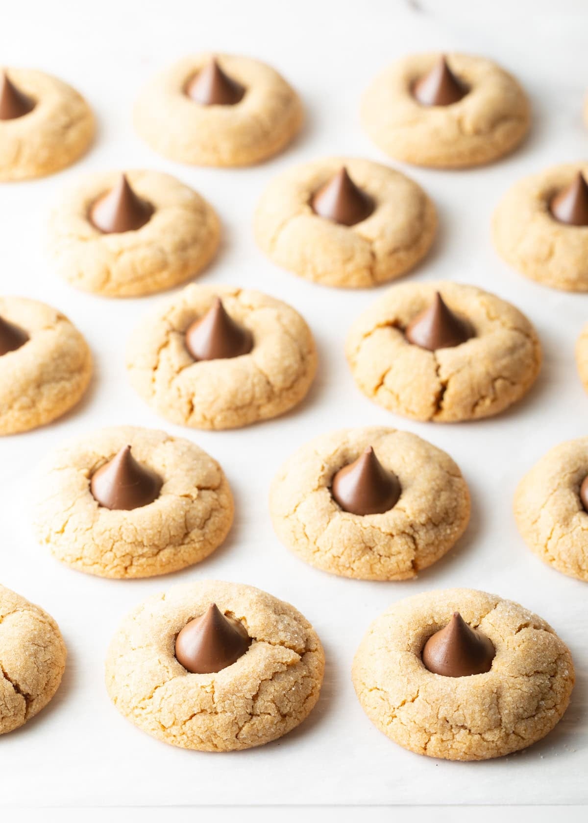 Peanut butter kiss cookies lined up on white parchment paper.