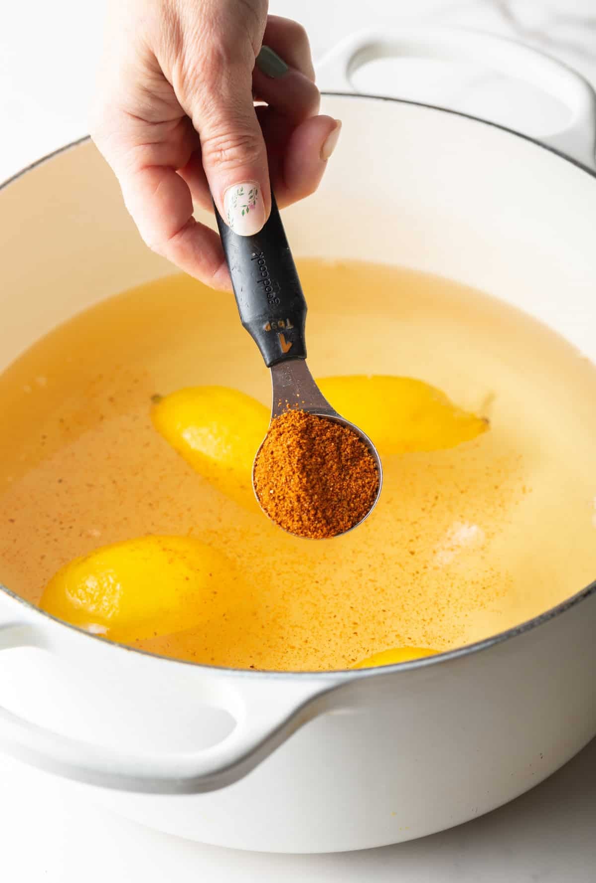 Old Bay seasoning is being added to a pot with lemon slices, water, and beer.