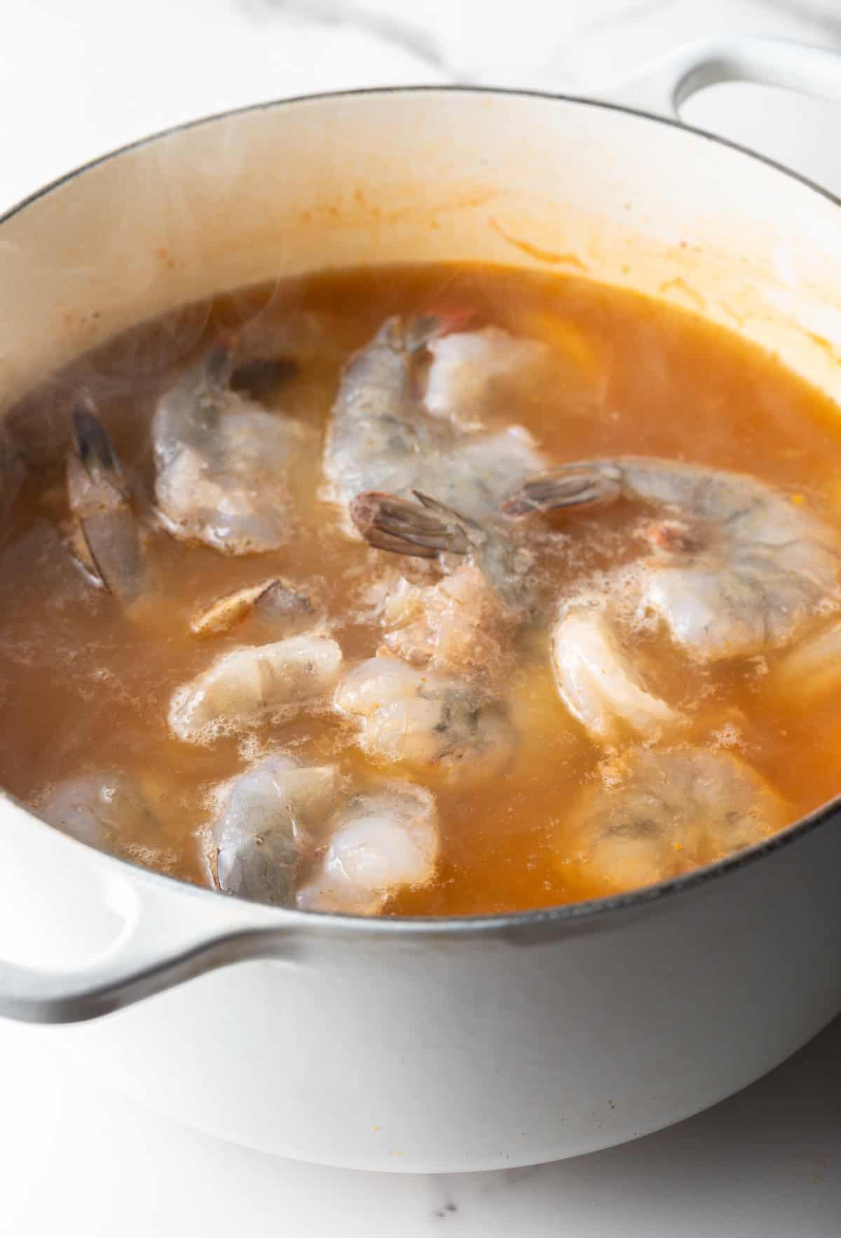 Raw shrimp has been added to a pot with a beer, lemon, and Old Bay-seasoned broth.