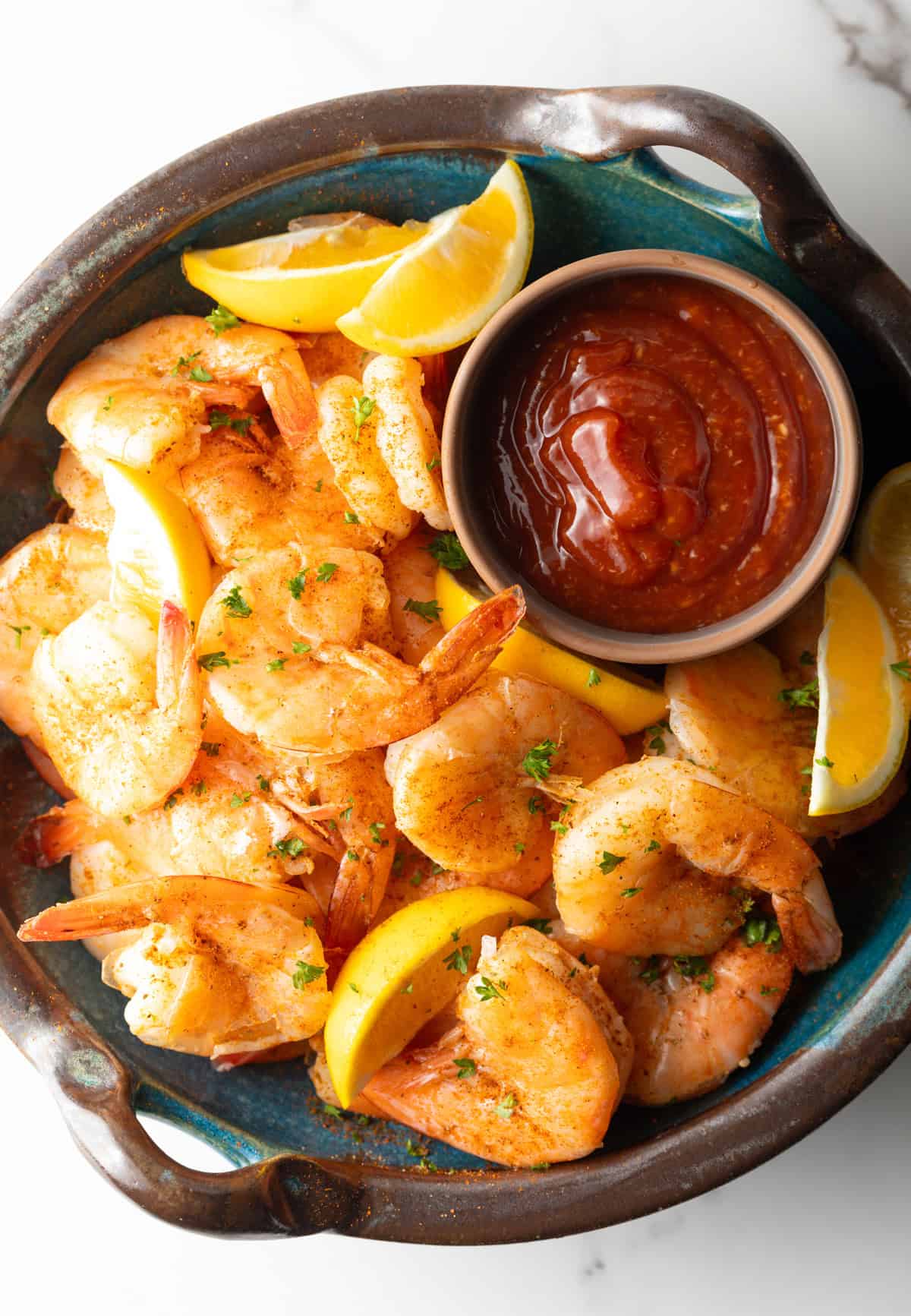 An overhead shot of a bowl filled with peel and eat shrimp, lemon wedges, and cocktail sauce.