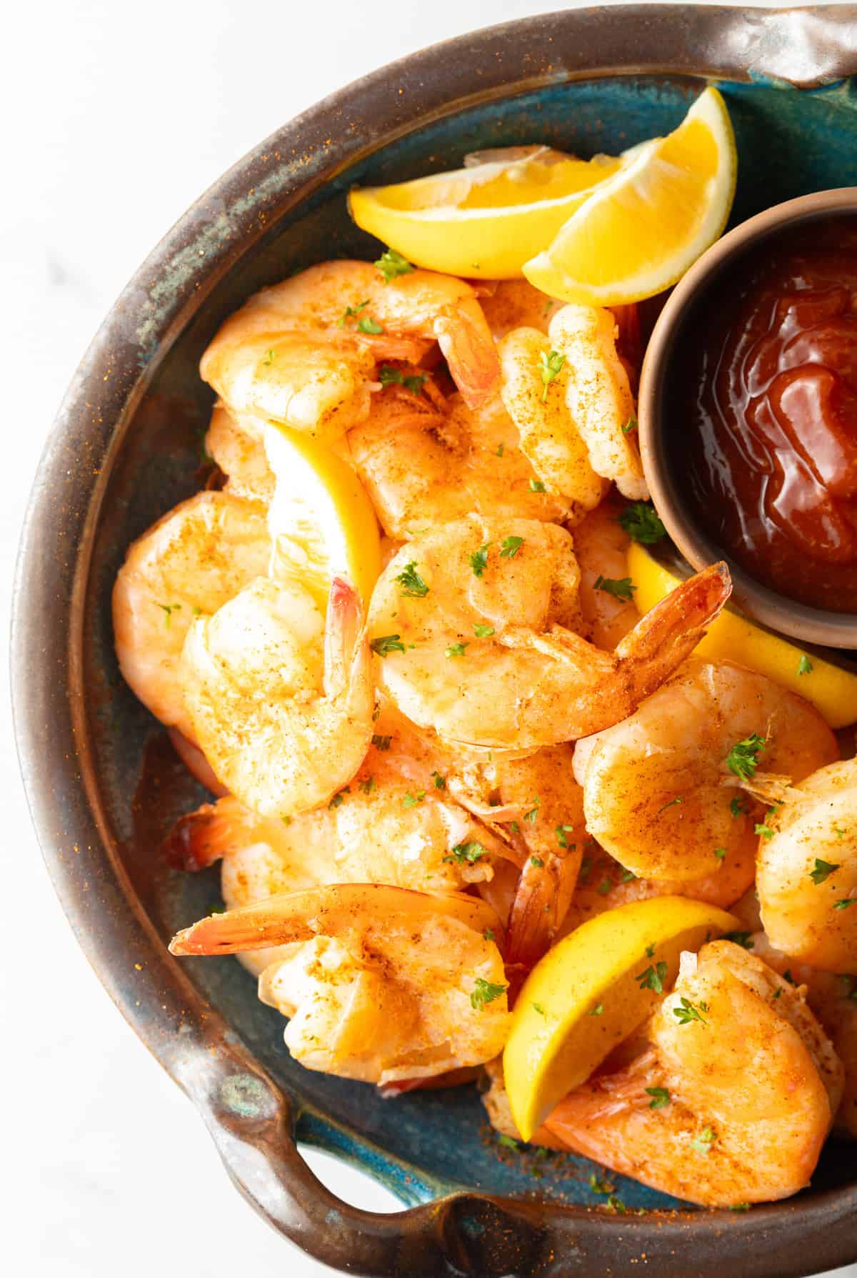 An overhead shot of easy peel and eat shrimp next to a ramekin of cocktail sauce and lemon wedges.
