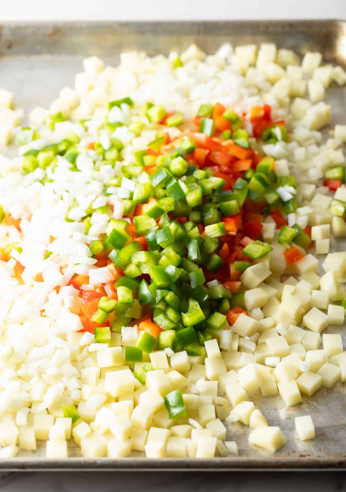 A baking sheet topped with diced potatoes, onions, and bell peppers.