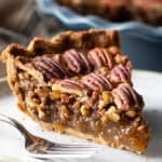 A close-up shot of a slice of simple pecan pie on a white plate.