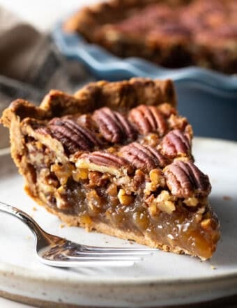 A close-up shot of a slice of simple pecan pie on a white plate.