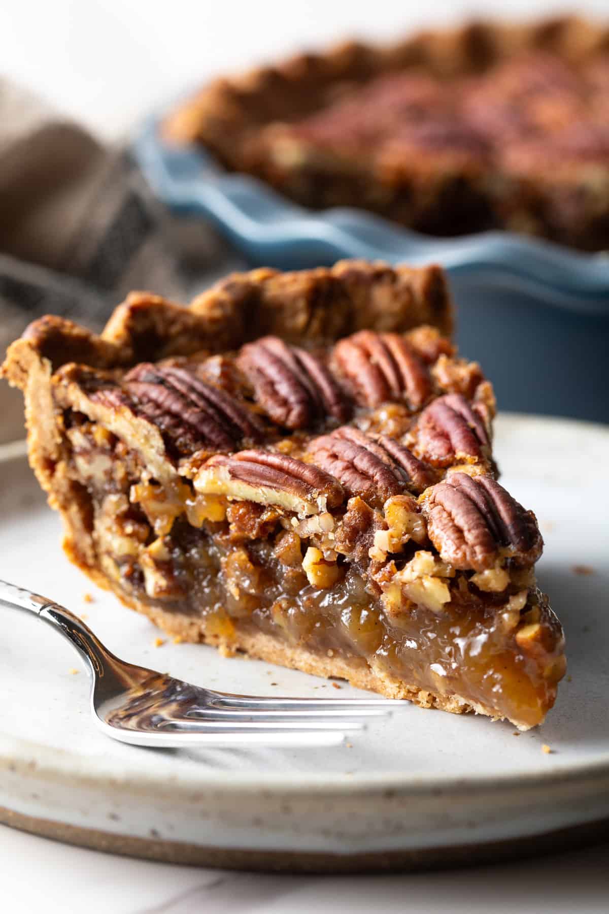 A close-up shot of a slice of simple pecan pie on a white plate.