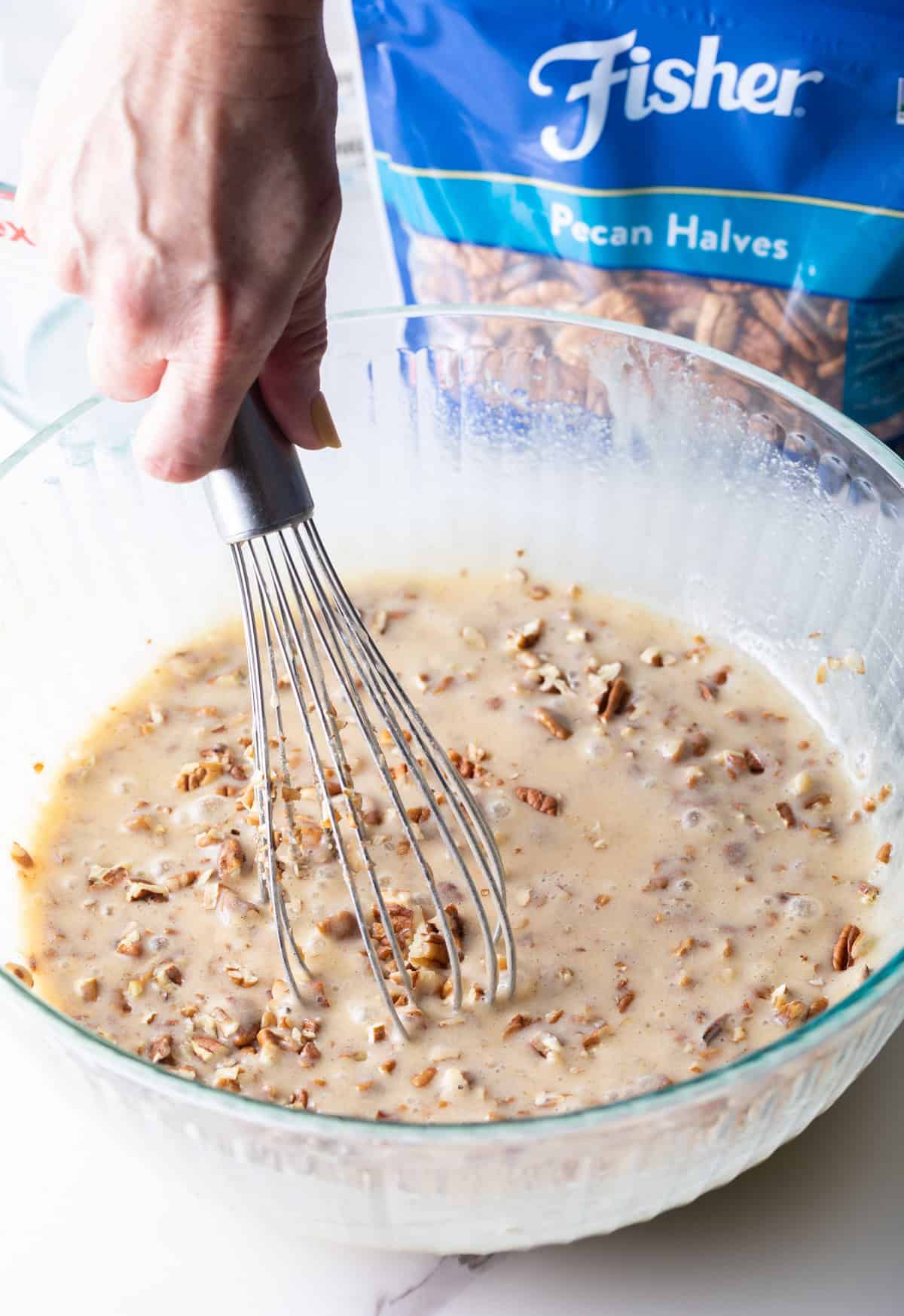 A pecan pie filling mixture is being whisked in a glass mixing bowl.