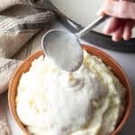 A white gravy recipe is being spooned over a bowl of mashed potatoes.