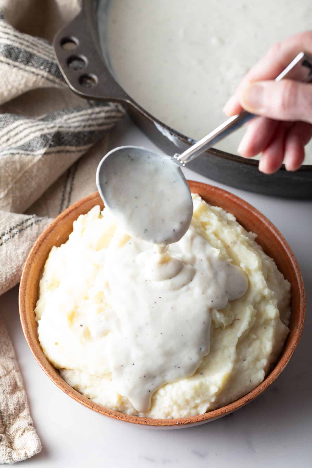A white gravy recipe is being spooned over a bowl of mashed potatoes.