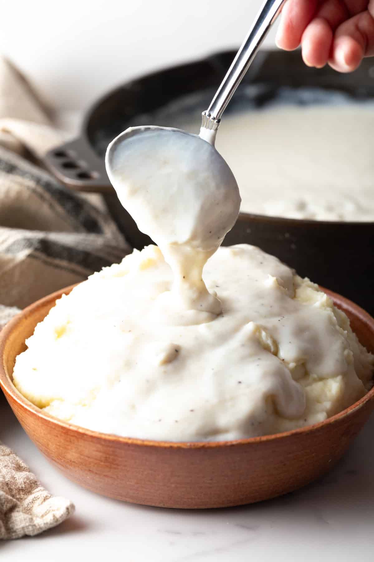 A homemade country gravy recipe is being spooned over a bowl of mashed potatoes.