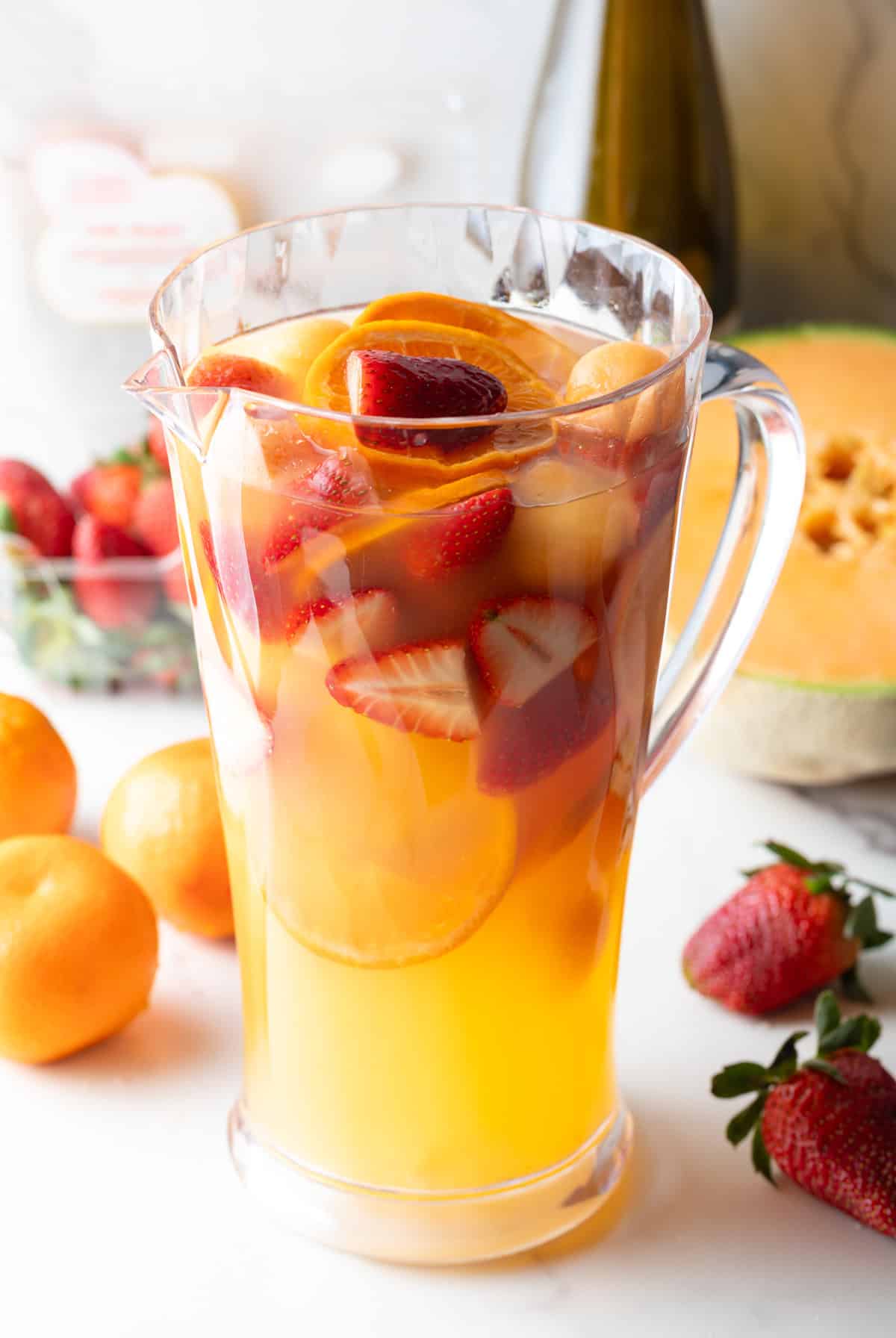 A class pitcher filled with freshly cut fruit and a white wine sangria cocktail.