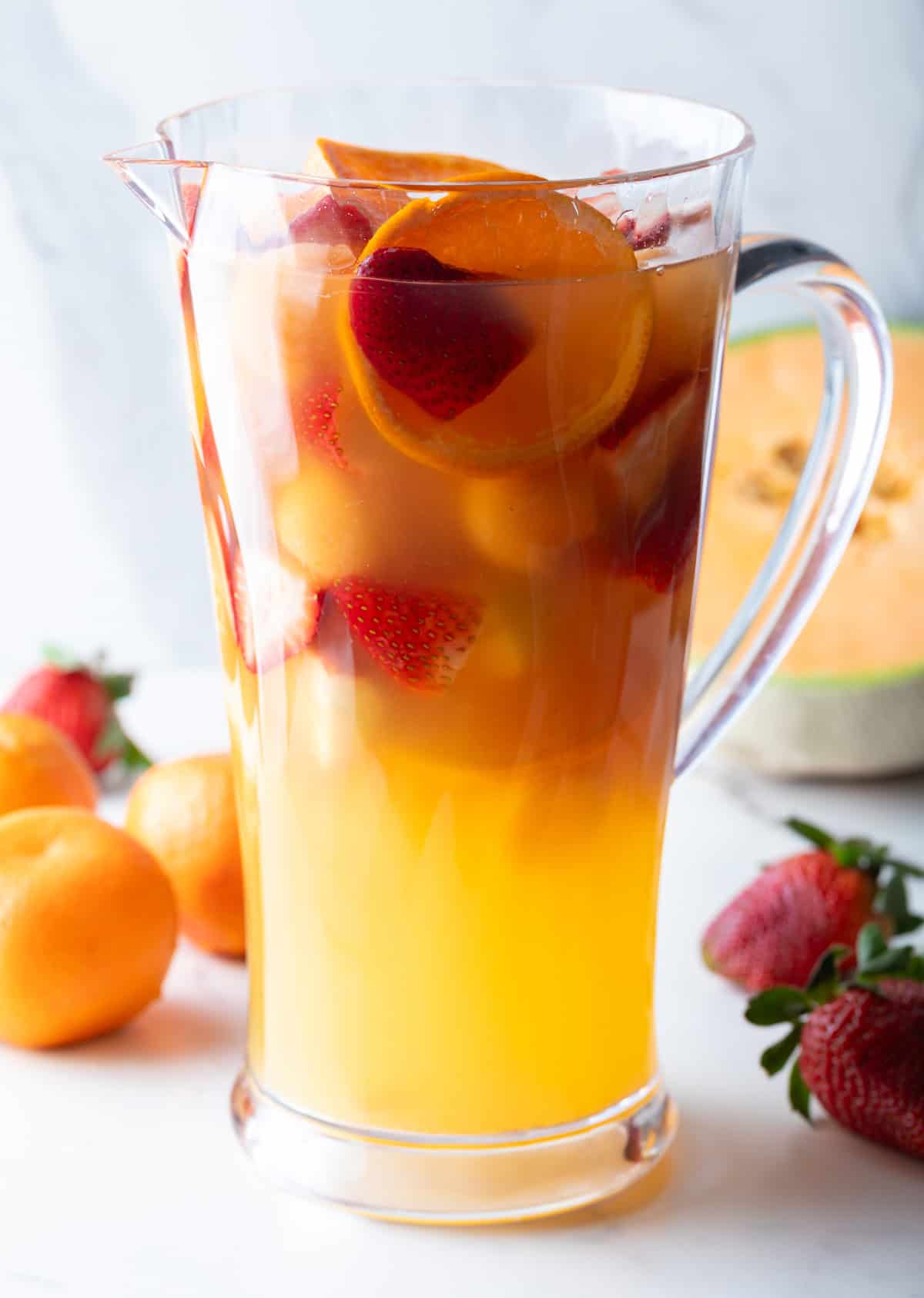 A glass pitcher filled with white wine sangria and fresh fruit slices.