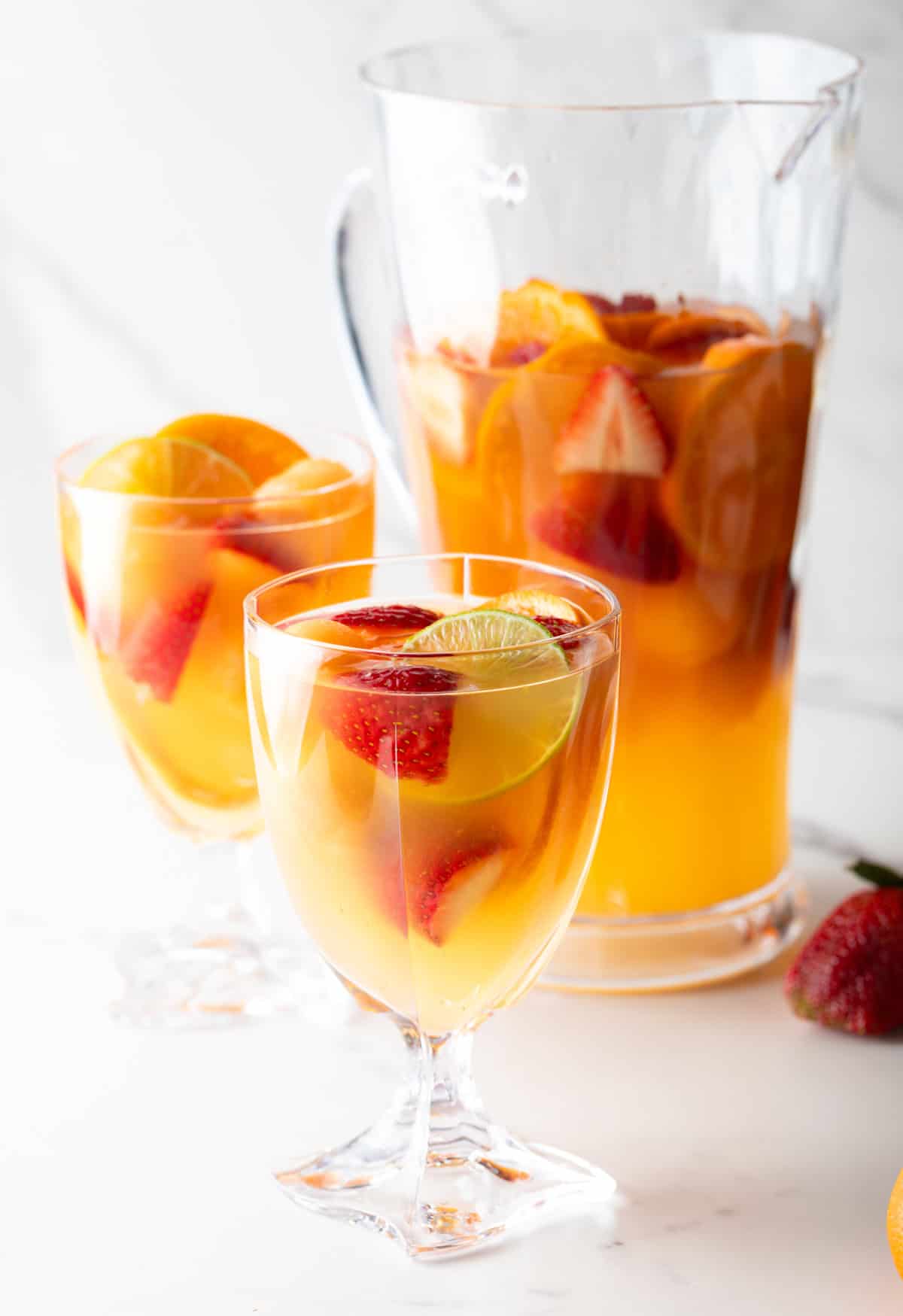 A pitcher and wine glasses filled with a white wine sangria recipe with fresh fruit floating in each.