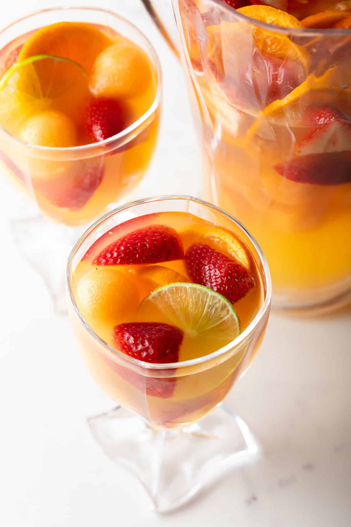 A wine glass filled with fruity wine sangria, next to a pitcher of the sangria.