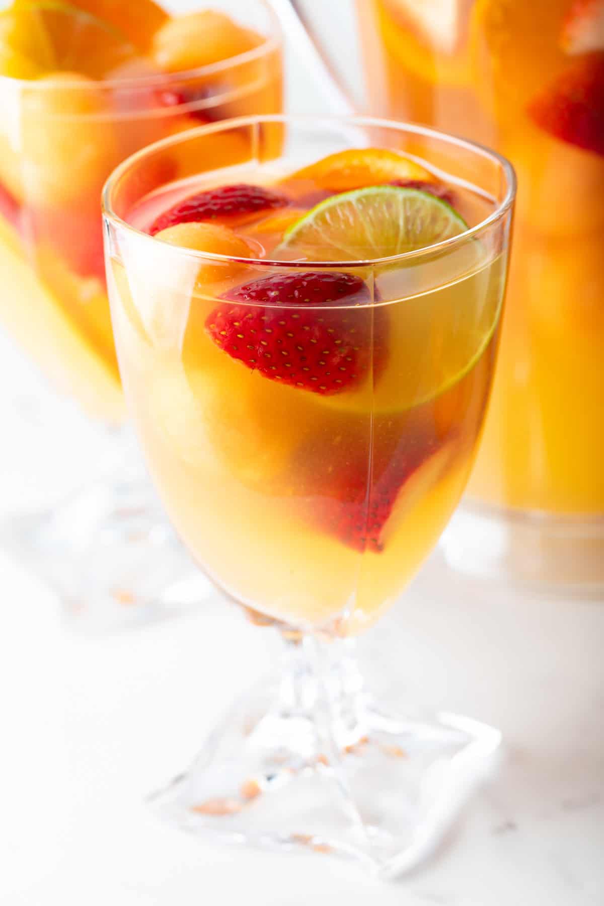 A wine glass filled with white sangria with fresh strawberries and orange slices.