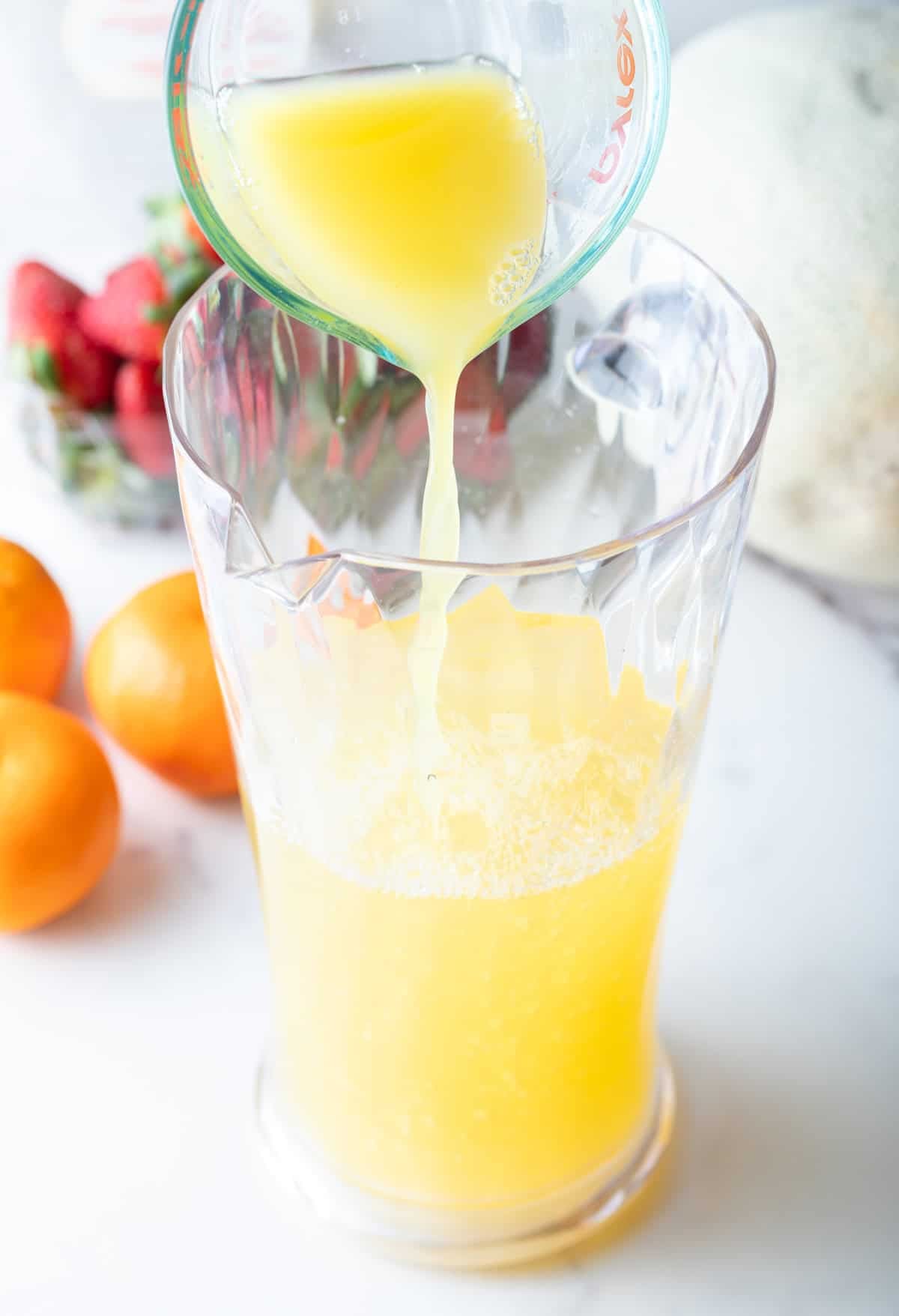 Orange juice is being added to a glass pitcher filled with a white sangria recipe.
