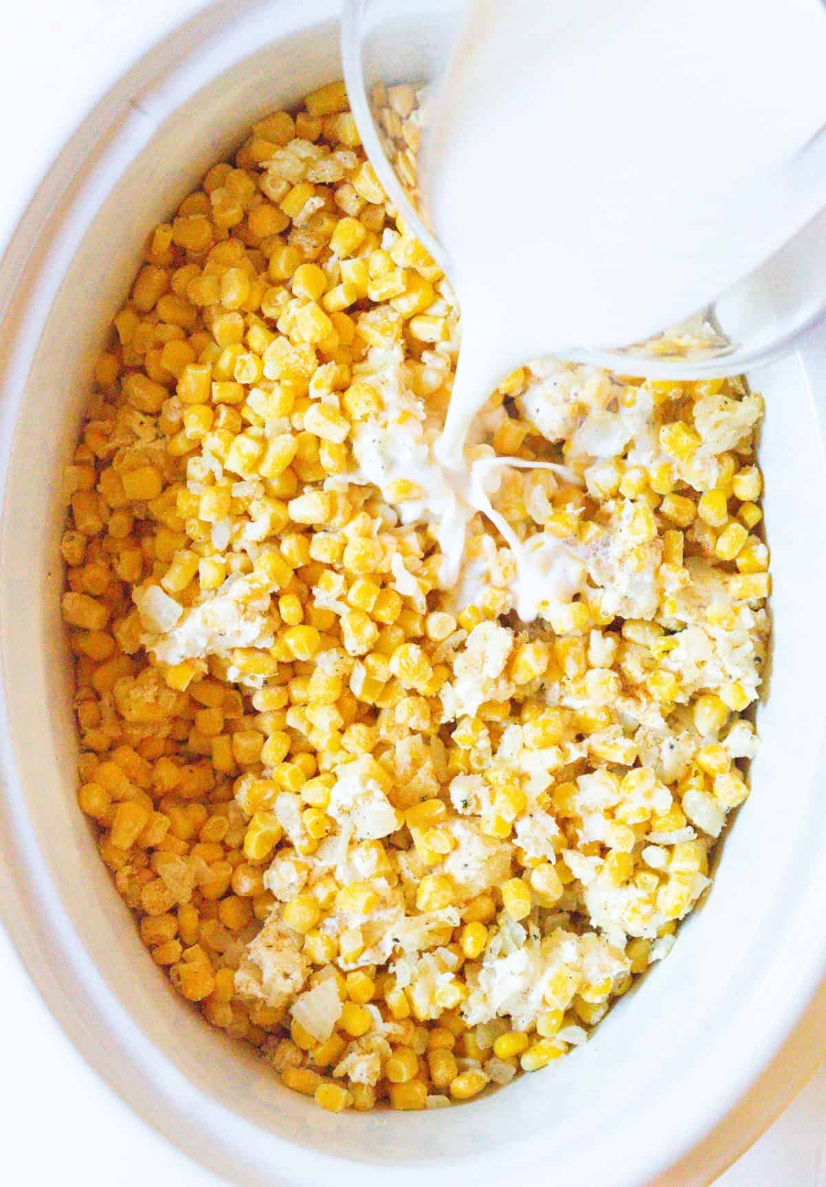 Milk is being added to a slow cooker creamed corn mixture.