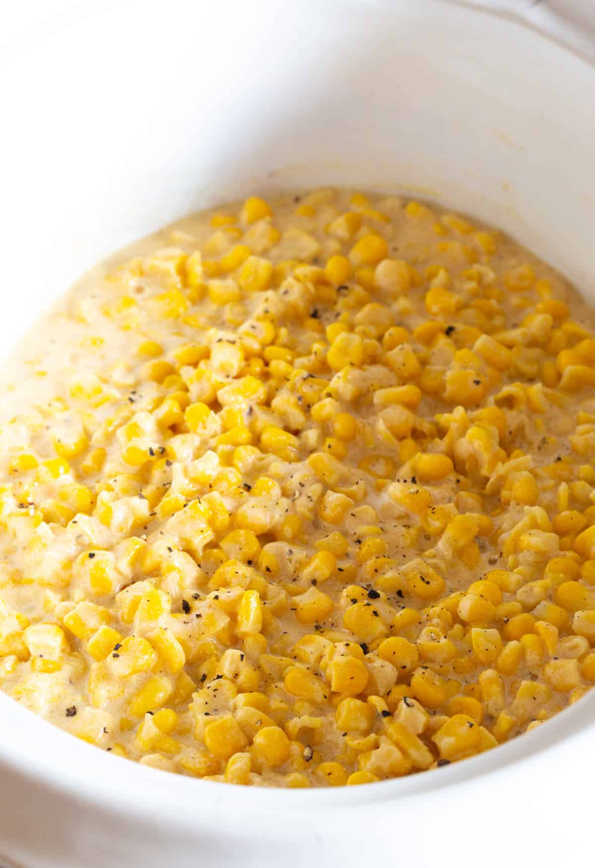 A simple crockpot creamed corn recipe sitting in a white crock.