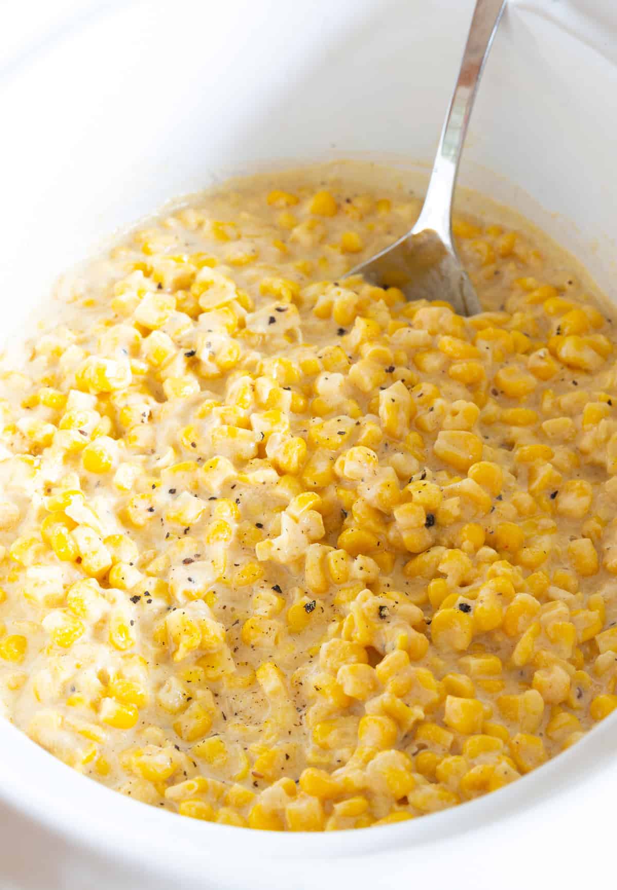 A crock pot creamed corn recipe sitting in a crock with a metal spoon.
