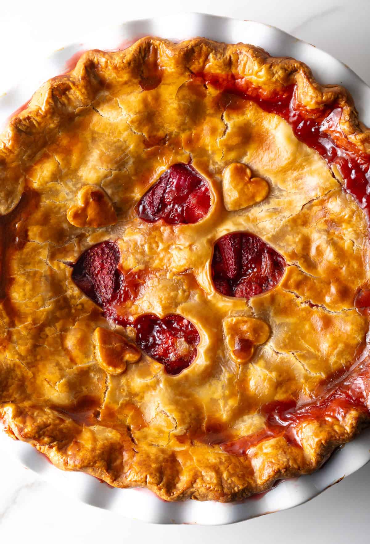 A freshly baked strawberry and rhubarb pie with heart shapes cut in the center of the pie.