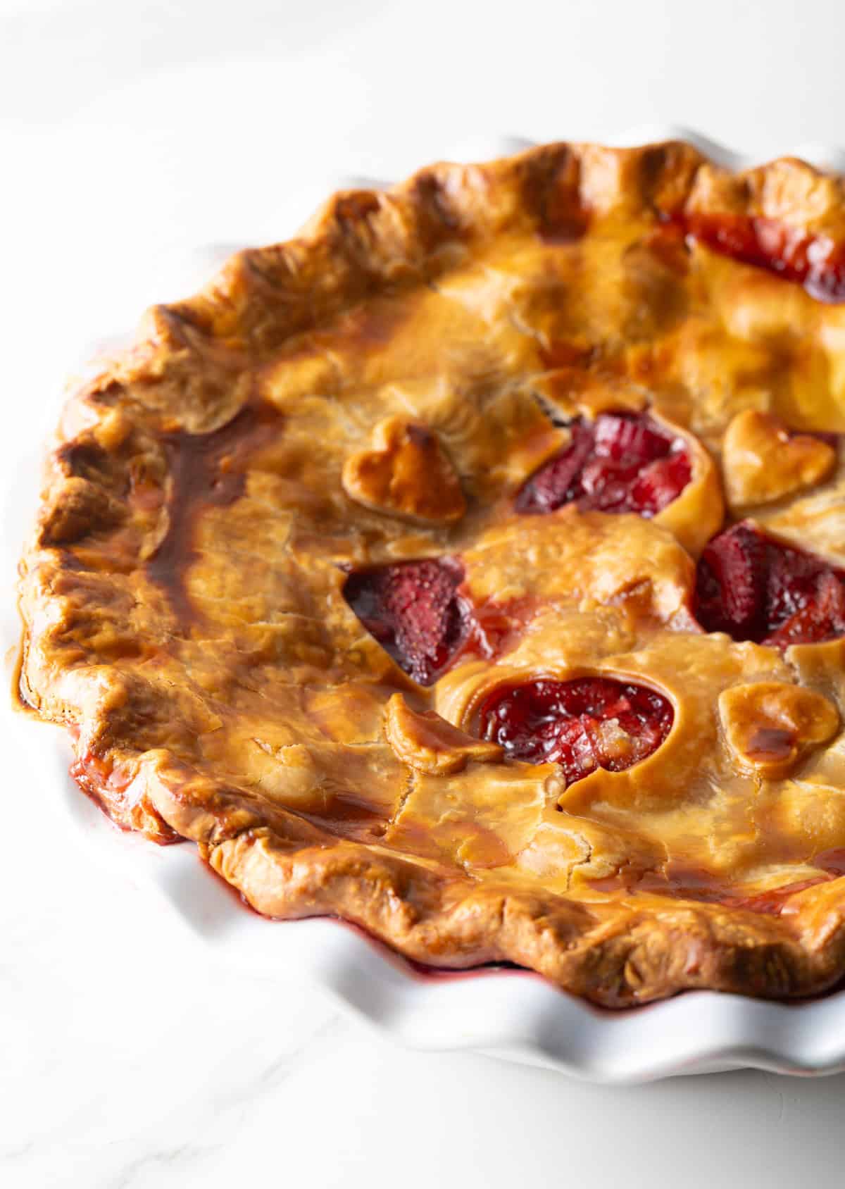 A full rhubarb strawberry pie with heart shapes cut in the center of the pie.