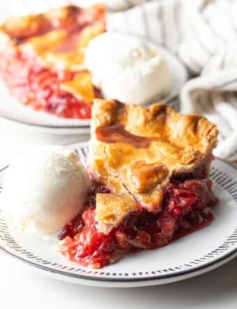 A slice of strawberry rhubarb pie with a scoop of vanilla ice cream on the side.