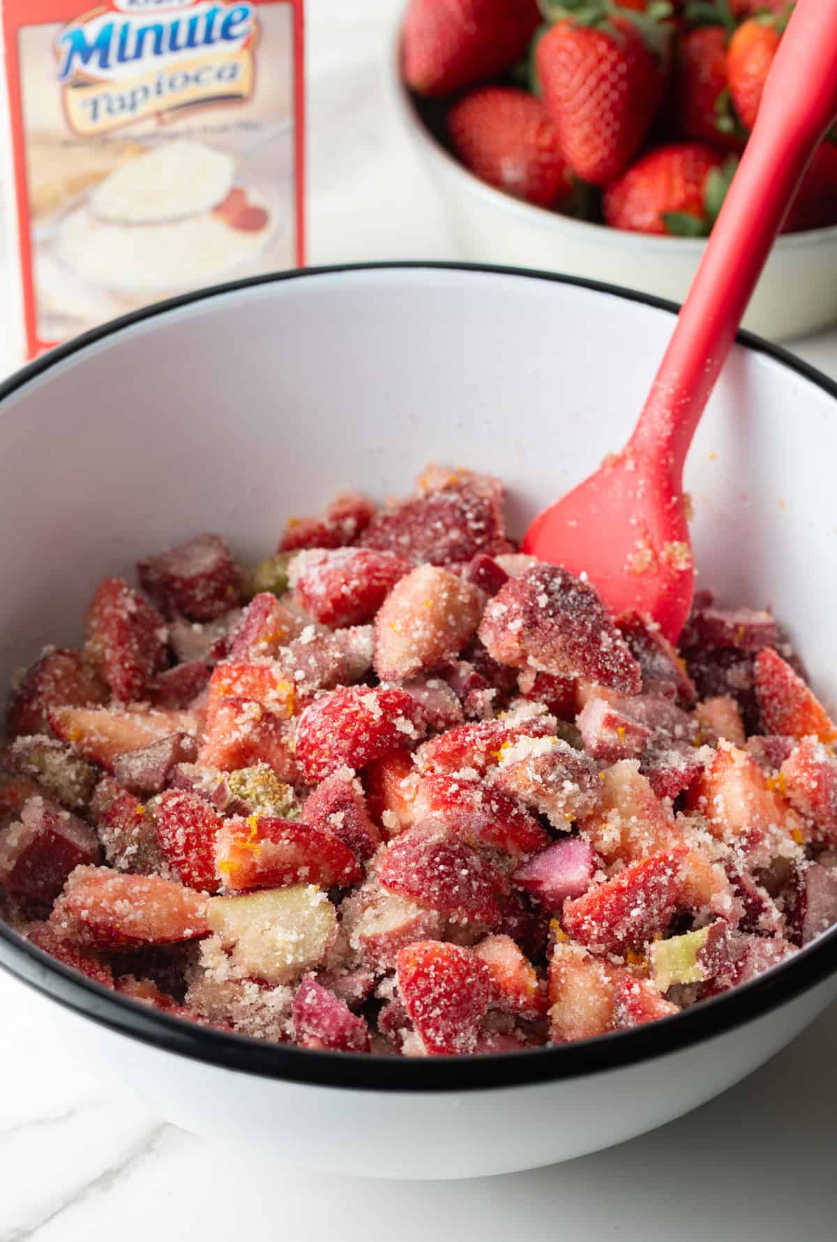 A strawberry rhubarb pie mixture is being stirred in a mixing bowl.
