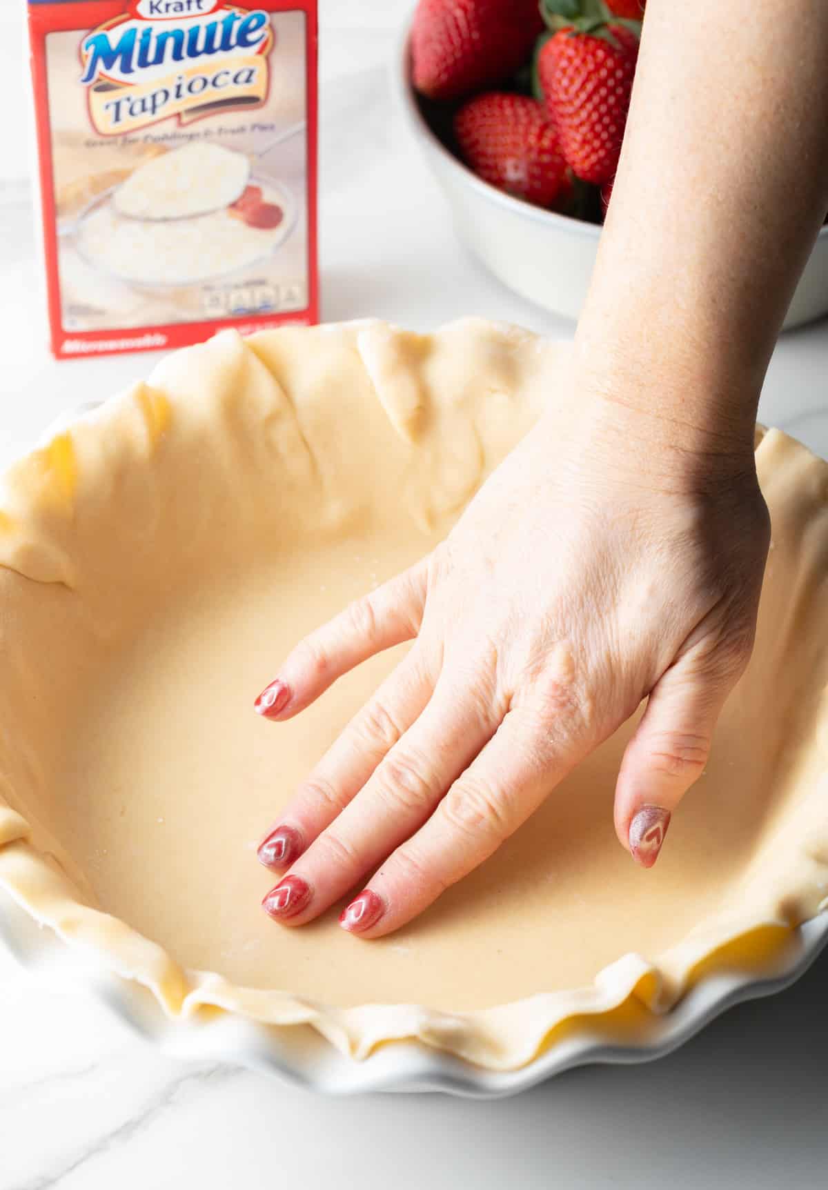 A hand is pressing a pie dough crust into a pie plate.